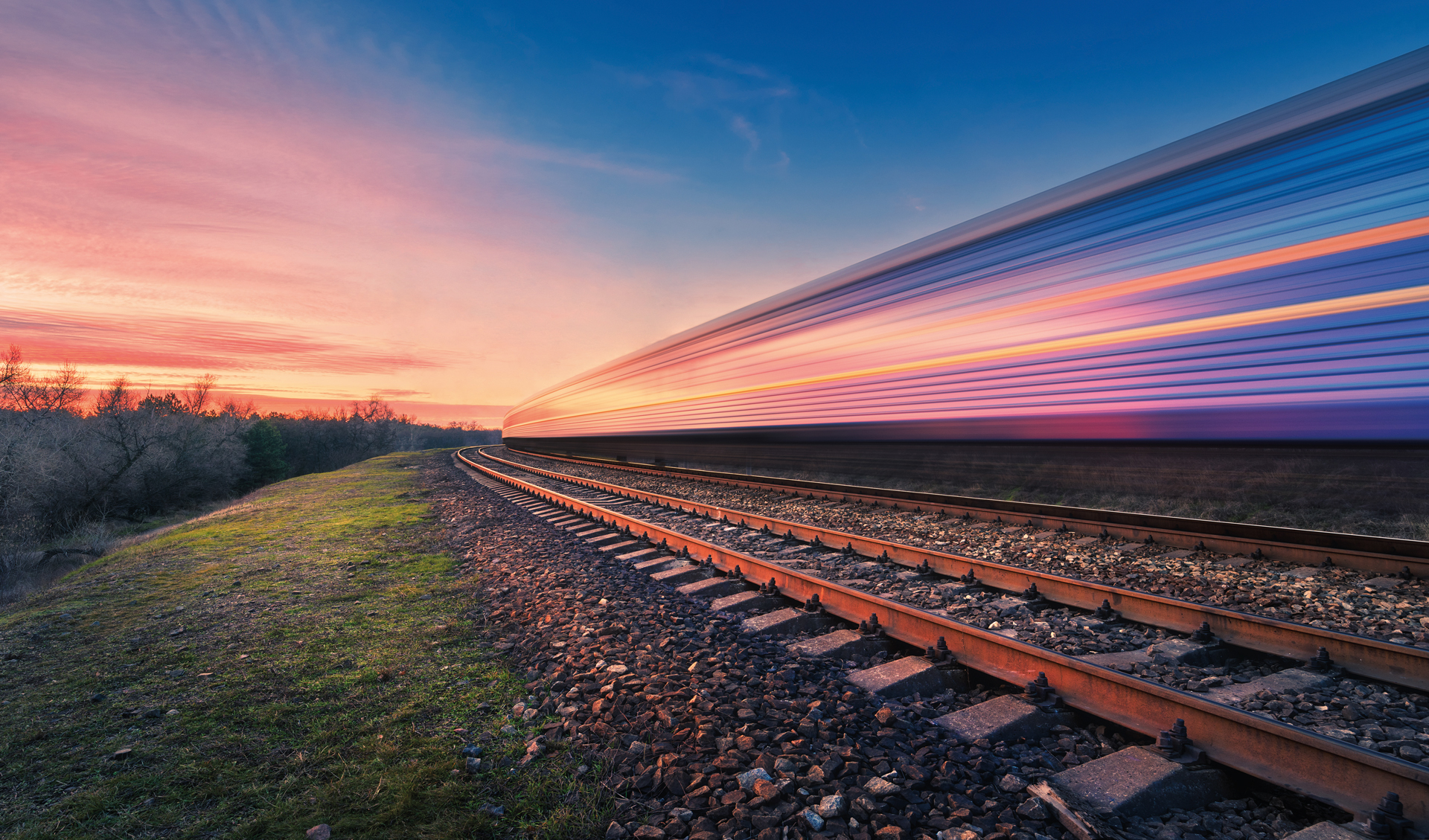 Railroad tracks with a train with trailing lights at dusk