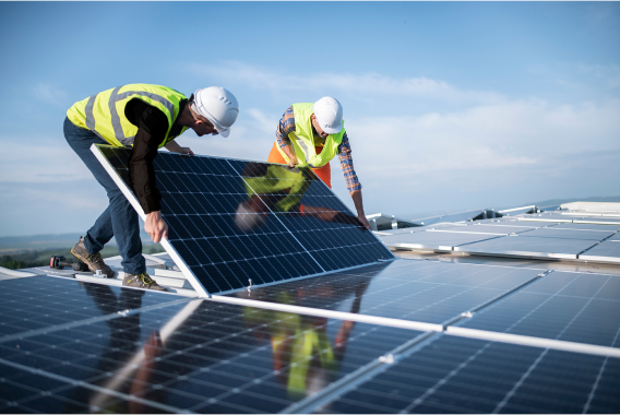 Workers with hardhat holding solar panel on top of a rooftop