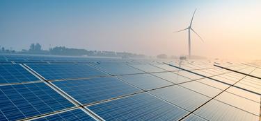 Solar panels at sunset with a wind turbine in the background