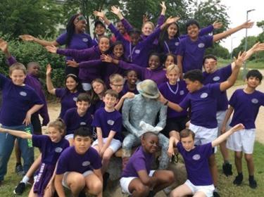 A group of young children dressed in purple surrounding a statute