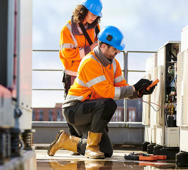 Two workers install an industrial air conditioner on top of a building